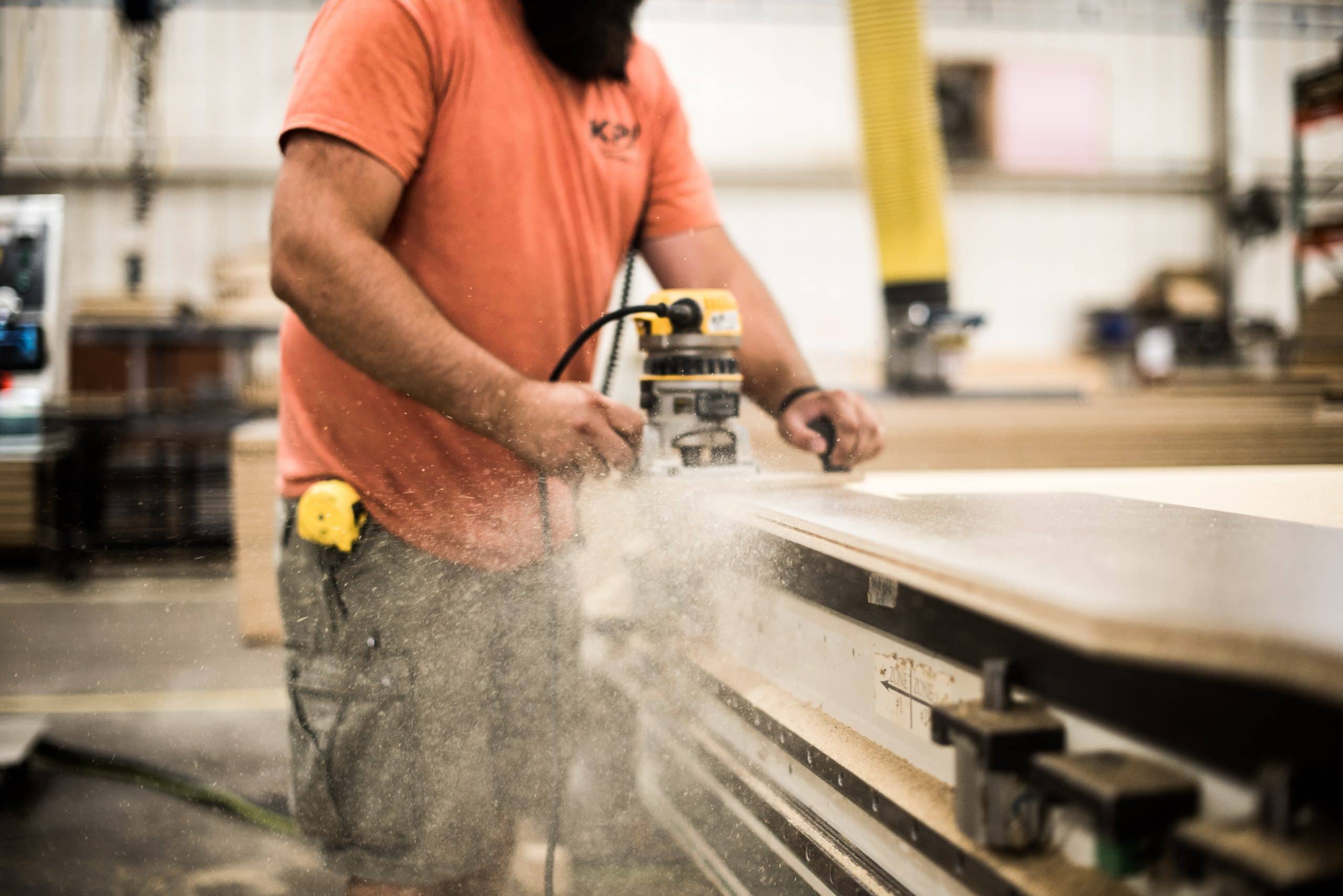 Kpi Concepts Worker Routing The Edge Of A Panel, With Sawdust Visible During The Process.
